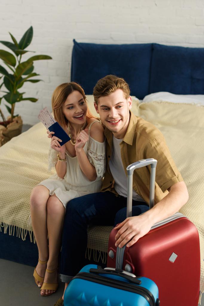 νεαρό ζευγάρι με τις βαλίτσες έτοιμες για διακοπές κάθεται στο κρεβάτι και κρατώντας τα διαβατήρια - Φωτογραφία, εικόνα