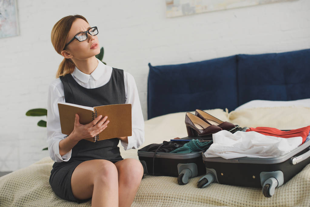 Nachdenkliche Geschäftsfrau hält Planer beim Kofferpacken im Bett - Foto, Bild