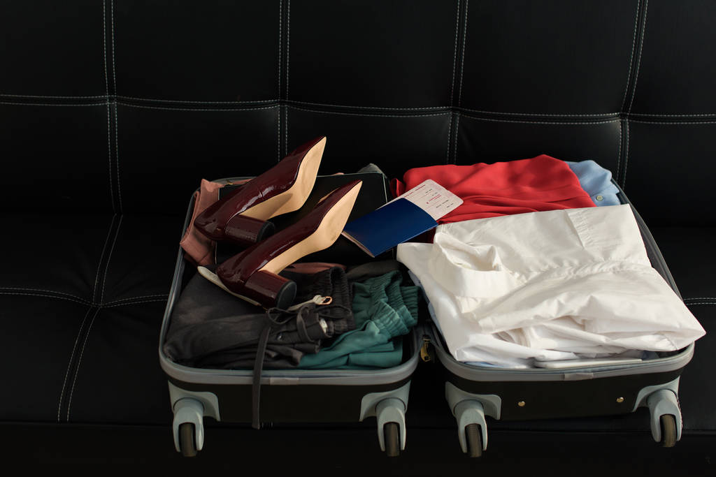 Reistas met paspoort, kleren en hakken op sofa geopend - Foto, afbeelding