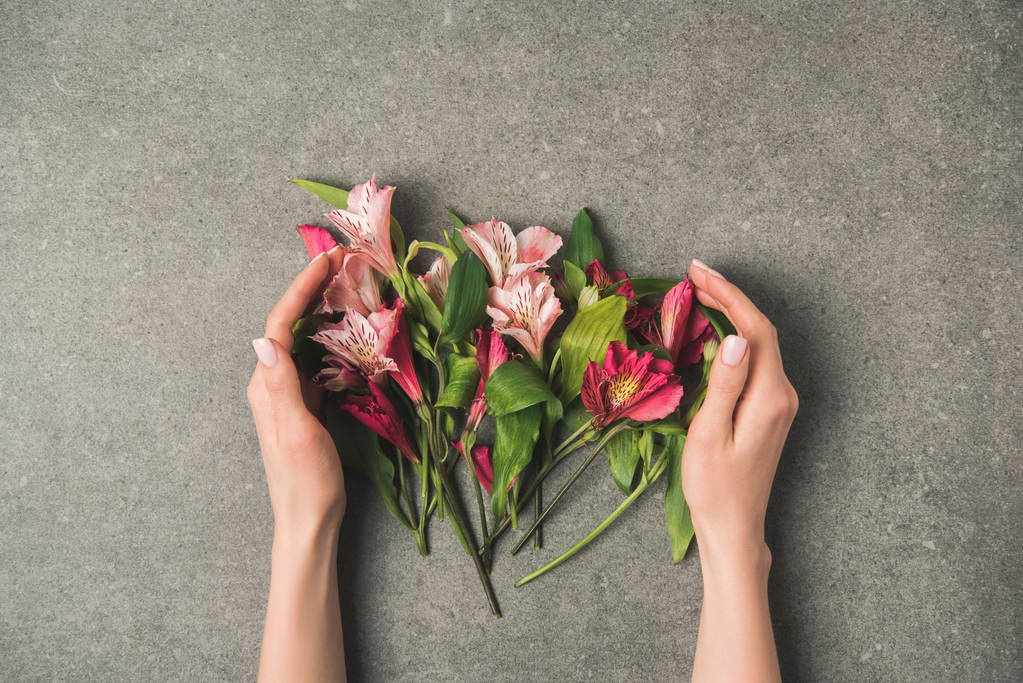 částečný pohled ženské ruce a krásné peruánské lilie na šedé betonové desky stolu - Fotografie, Obrázek