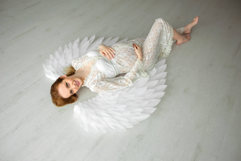 belle jeune fille enceinte aux cheveux roux dans une robe blanche dentelle couchée sur un sol clair
 - Photo, image