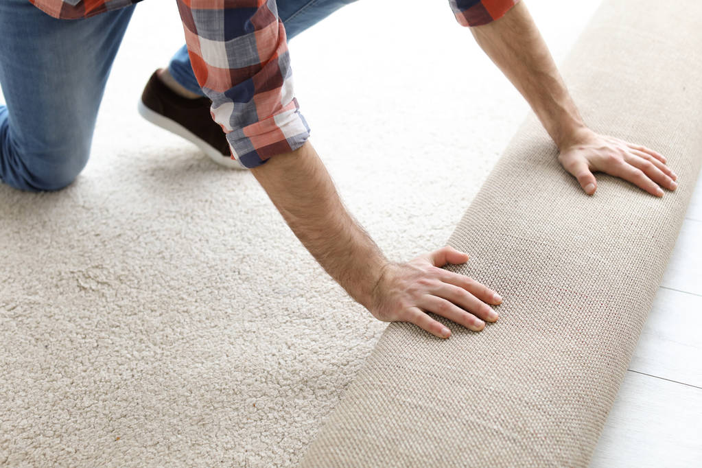 Hombre rodando nuevo suelo de alfombra en la habitación
 - Foto, Imagen
