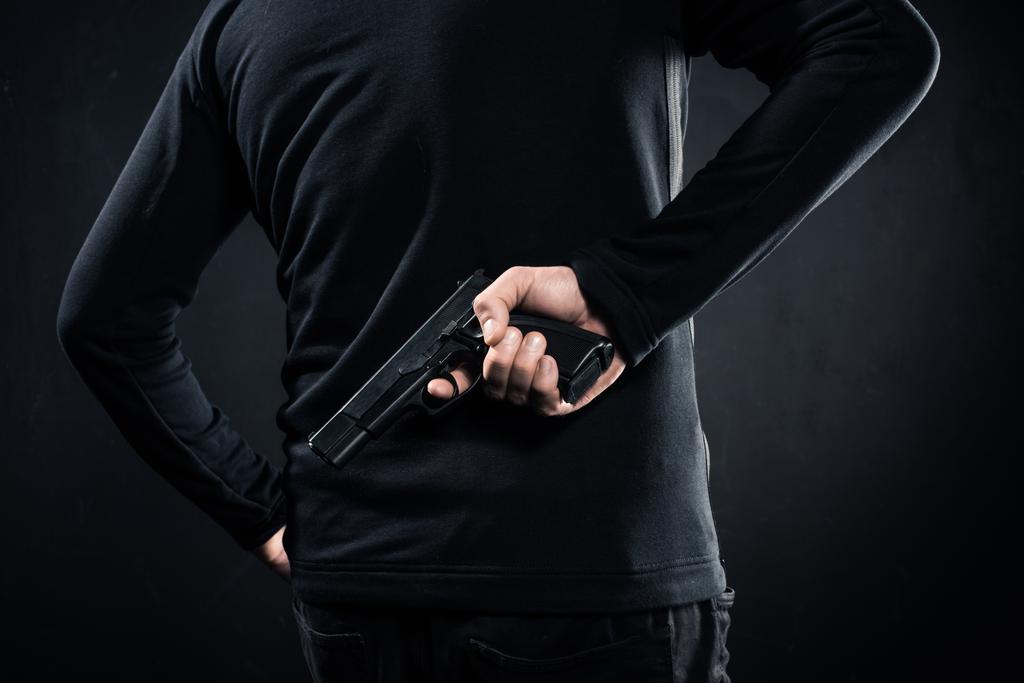 Achteraanzicht van pistool in handen van gangster op zwart - Foto, afbeelding