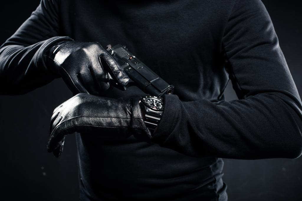 Hombre en guantes con pistola revisando su reloj
  - Foto, Imagen