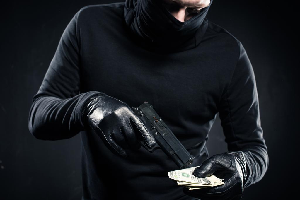 Homme en cagoule noire tenant pistolet et dollars
 - Photo, image