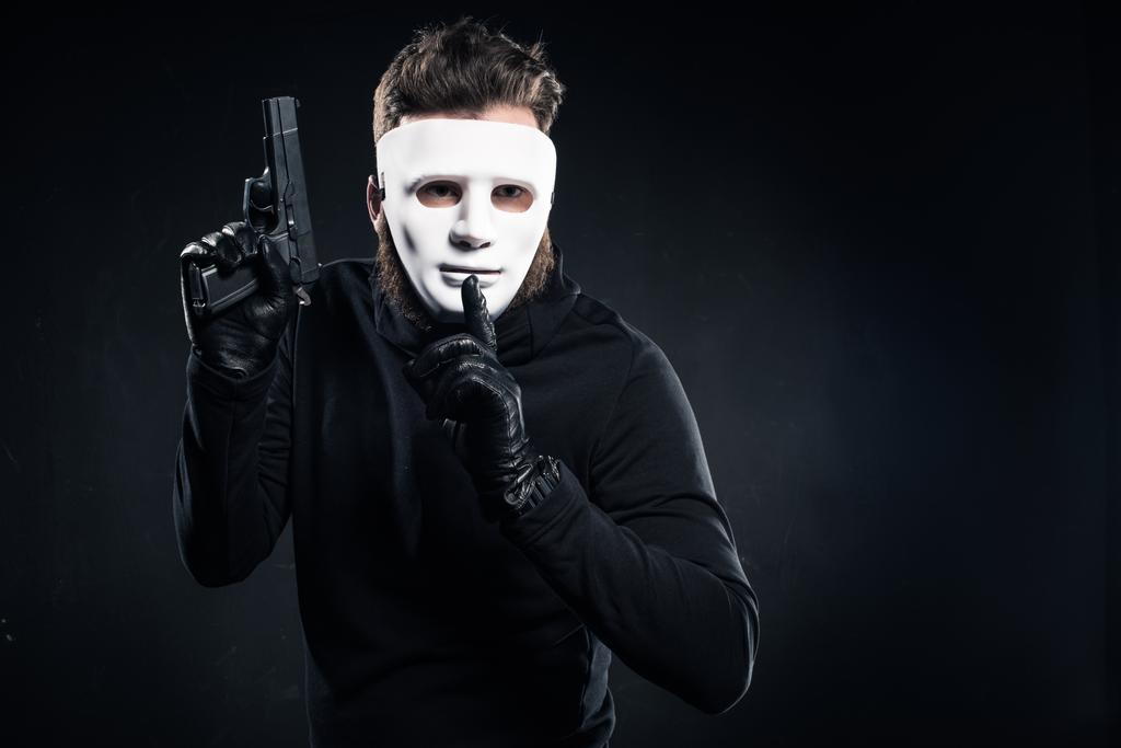Κλέφτης στη μάσκα κρατώντας όπλο και δείχνοντας σιωπή χειρονομία - Φωτογραφία, εικόνα