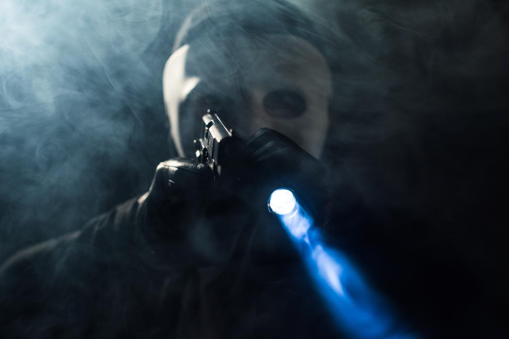 Criminal in masker en balaclava gericht met pistool en flitslicht - Foto, afbeelding