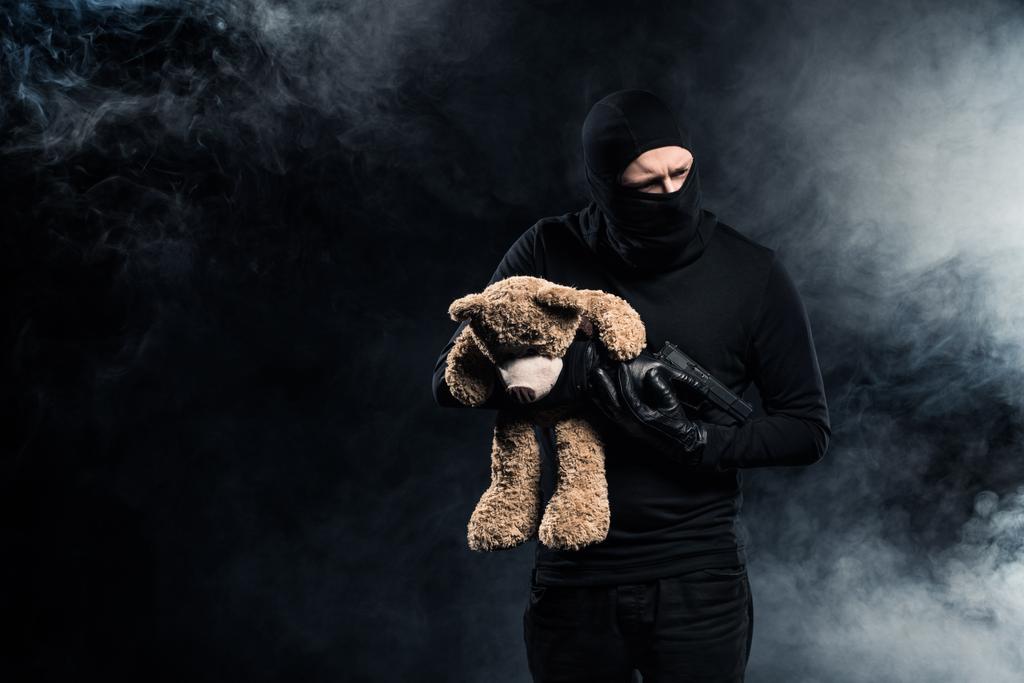 Похититель в балаклаве с пистолетом и плюшевым мишкой
 - Фото, изображение