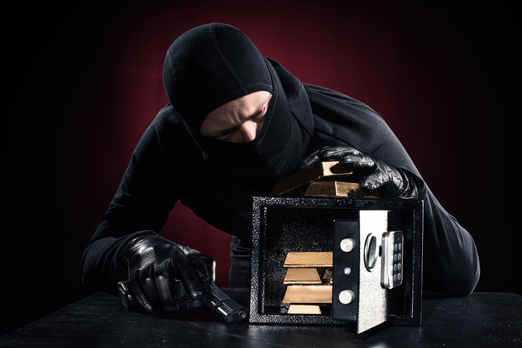 Hombre en pasamontañas con pistola robando lingotes de oro de caja fuerte
 - Foto, imagen
