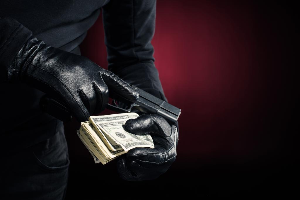 Przycięte widok pistolet i dolarów w rękach zbójnika - Zdjęcie, obraz
