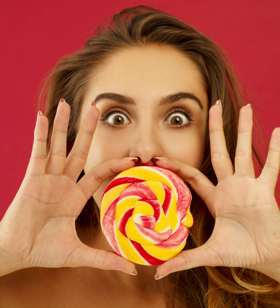 Retrato de una chica bonita feliz sosteniendo dulces sobre bac rojo
 - Foto, imagen