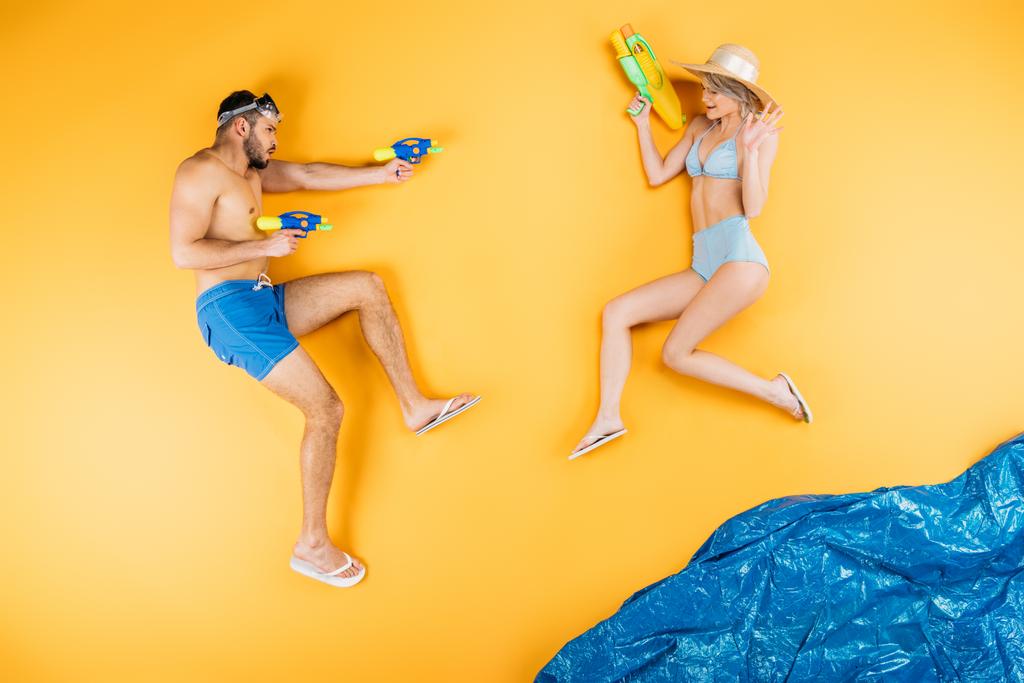 pareja joven en traje de baño jugando con pistolas de agua en imaginar playa, concepto de vacaciones de verano
 - Foto, Imagen