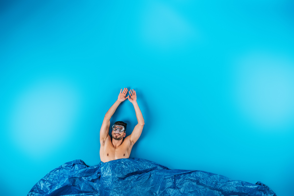 happy young man in swimming mask raising hands from imagine waves on blue - Photo, Image