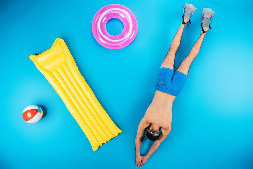 вид сверху молодого человека, ныряющего с ластами и пляжными вещами на голубом фоне
 - Фото, изображение