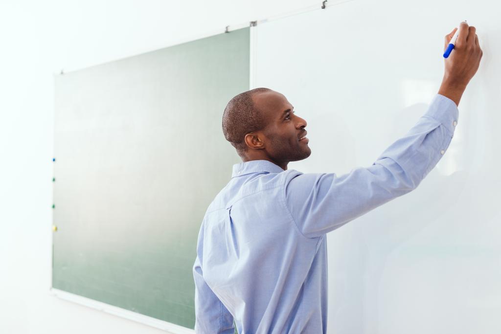 Lächelnder afrikanisch-amerikanischer Lehrer, der auf Whiteboard im Klassenzimmer schreibt - Foto, Bild