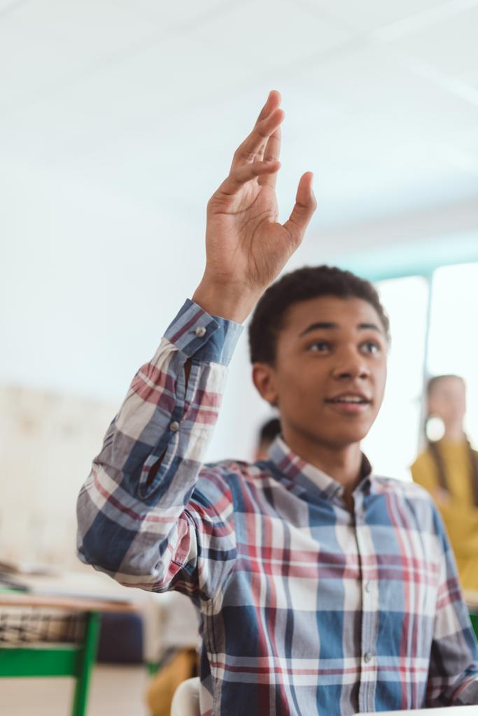 African american teenage student with arm up and classmates behind in classroom  - Photo, Image