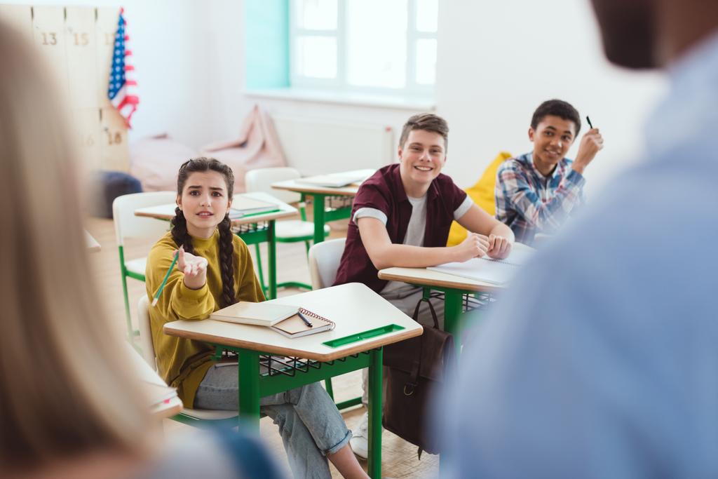 Обрізане зображення вчителя зі школяркою і однокласниками, що сидять за столами
  - Фото, зображення