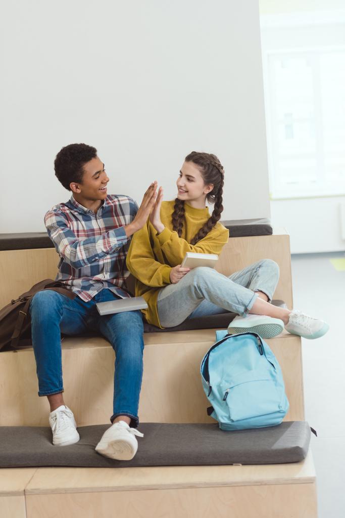 high school students couple sitting together at school corridor and giving high five - Photo, Image