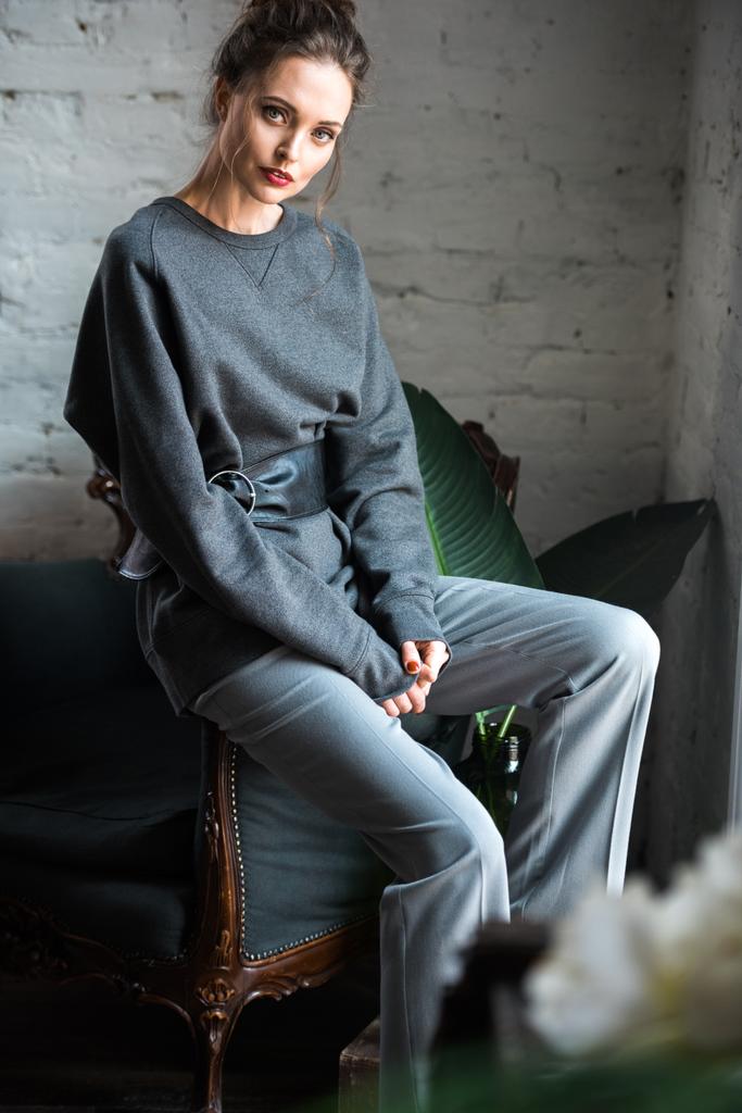 kaunis nuori nainen trendikkäissä harmaissa vaatteissa istuu nojatuolissa ja katselee kameraa
 - Valokuva, kuva