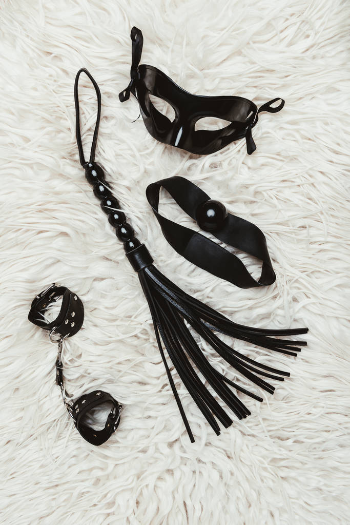 Zwarte bdsm gag met zweep en masker op witte tapijt - Foto, afbeelding