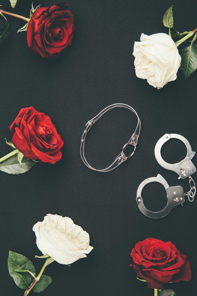 Kragen und Handschellen mit Rosenblüten isoliert auf schwarz - Foto, Bild