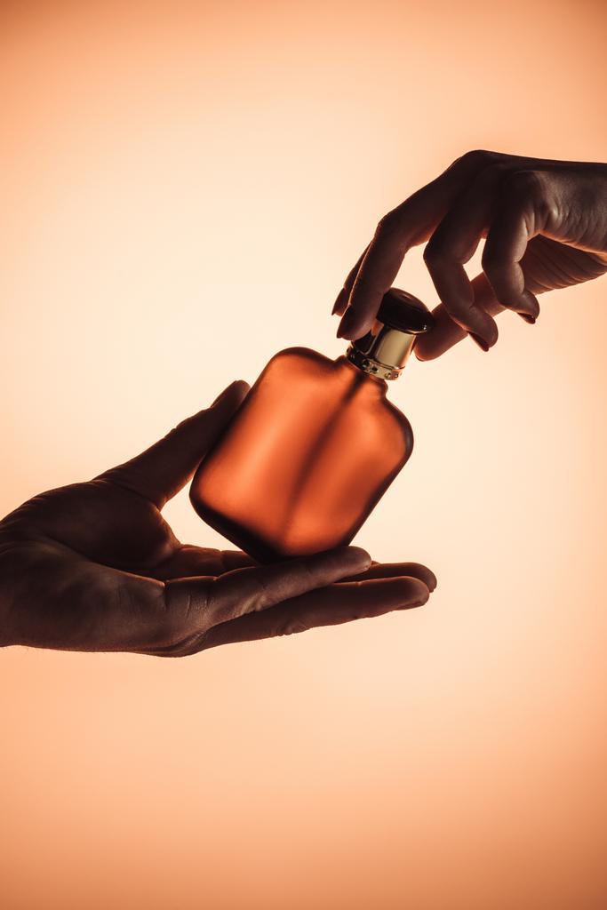 περικοπεί προβολή των αρσενικών και θηλυκών χεριών με μπουκάλι άρωμα, απομονώνονται σε πορτοκαλί  - Φωτογραφία, εικόνα