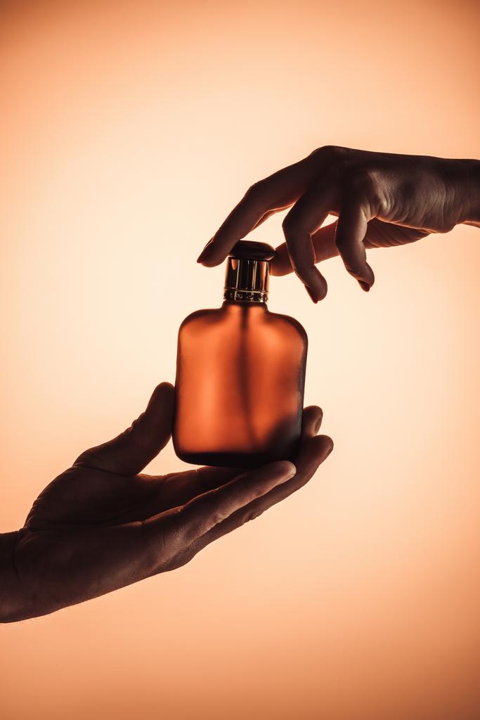περικοπεί άποψη του άνδρα και της γυναίκας που κρατάει ένα μπουκάλι του αρώματος, απομονώνονται σε πορτοκαλί  - Φωτογραφία, εικόνα