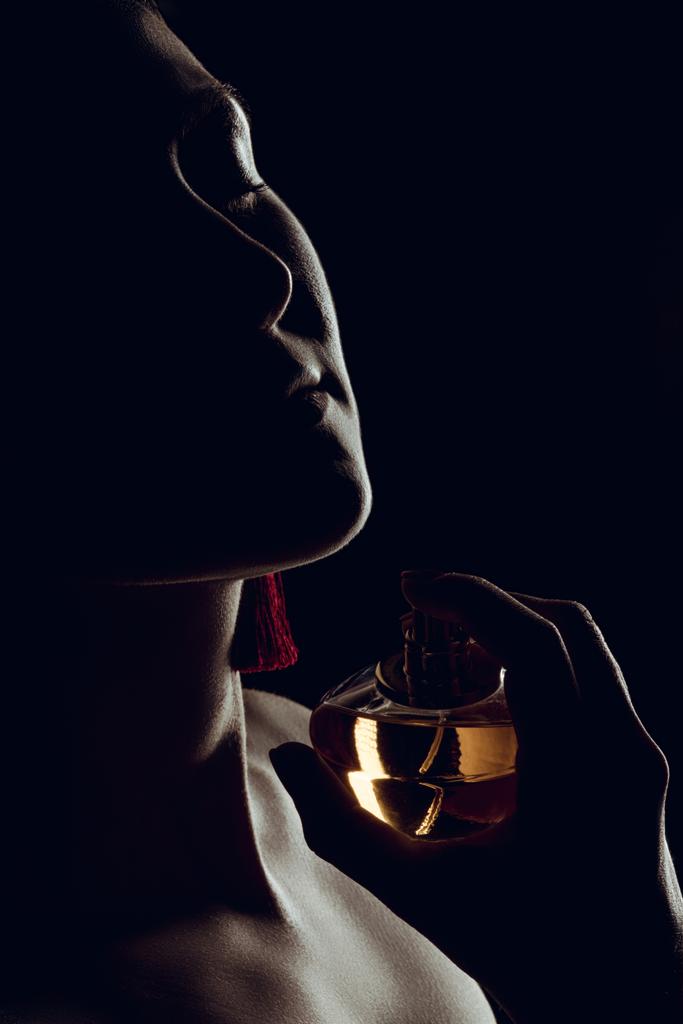 Silhouette einer sinnlichen Frau, die Parfüm auf den Hals sprüht, isoliert auf Schwarz - Foto, Bild