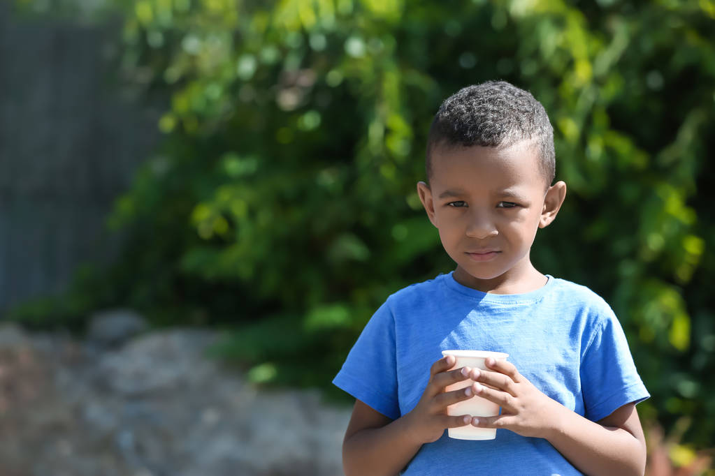 かわいいアフリカ系アメリカ人の男の子、屋外のプラスチック製のコップから水を飲む - 写真・画像