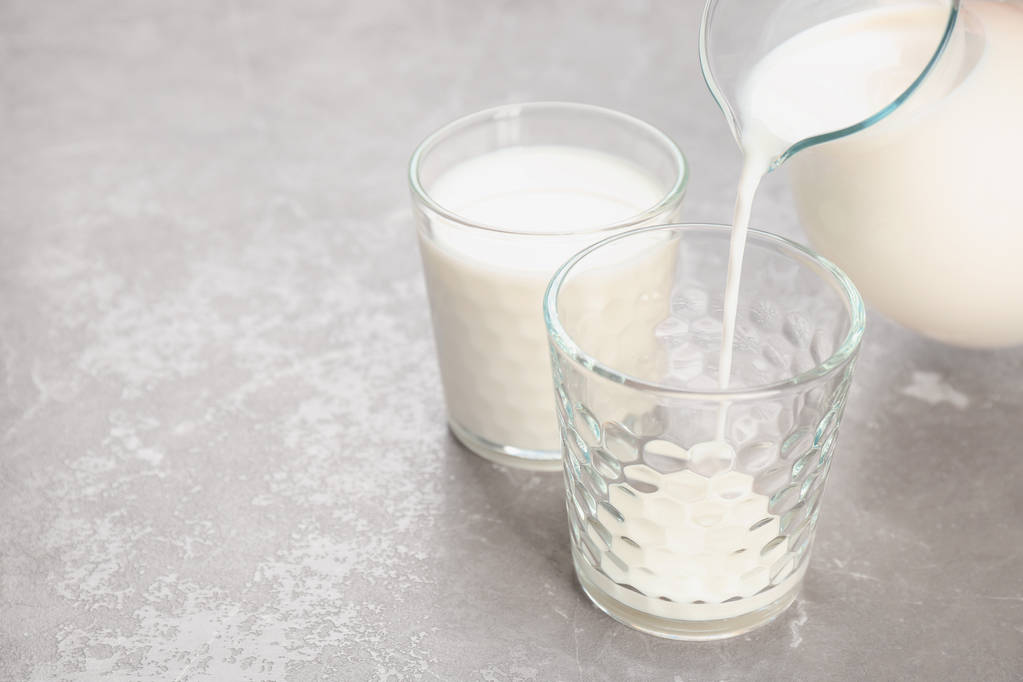Pouring of milk from jug into glass on table. Fresh dairy product - Photo, Image