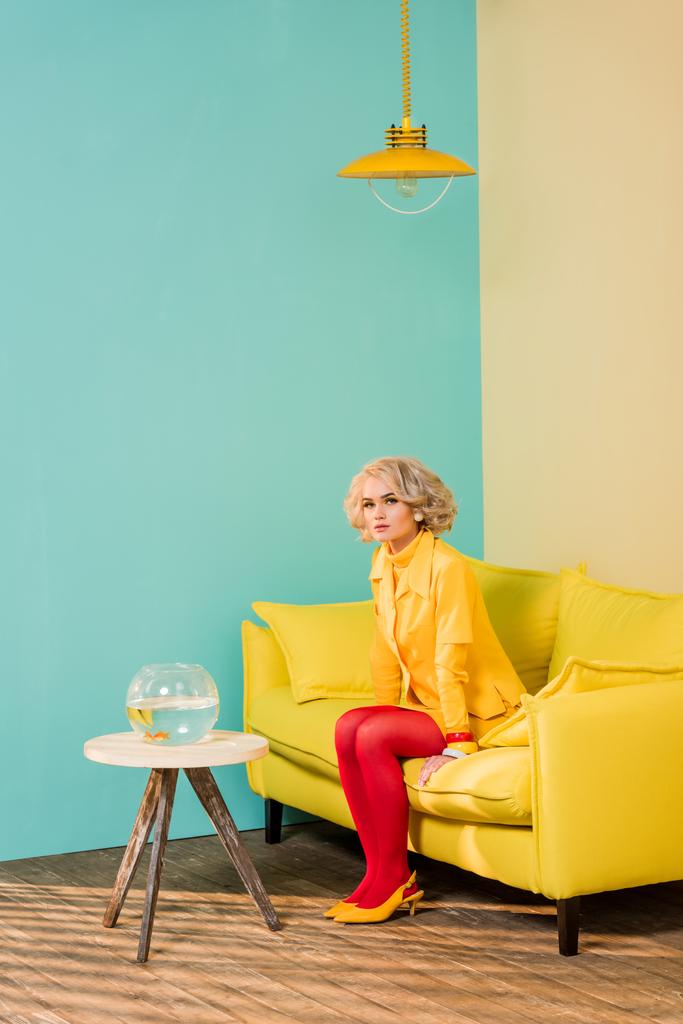 γυναίκα στο φωτεινό ρετρό ρούχα ακουμπά στον καναπέ στο πολύχρωμο διαμέρισμα, κούκλα σπίτι έννοια - Φωτογραφία, εικόνα