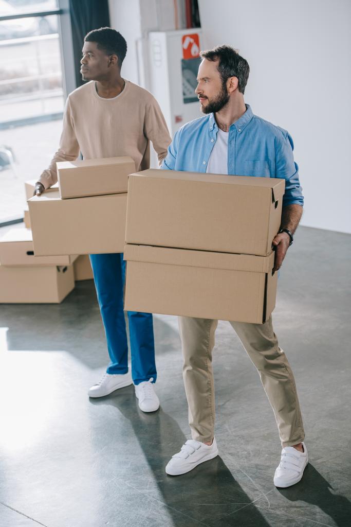 высокий угол обзора молодых мультиэтнических мужчин, держащих картонные коробки во время переселения
 - Фото, изображение