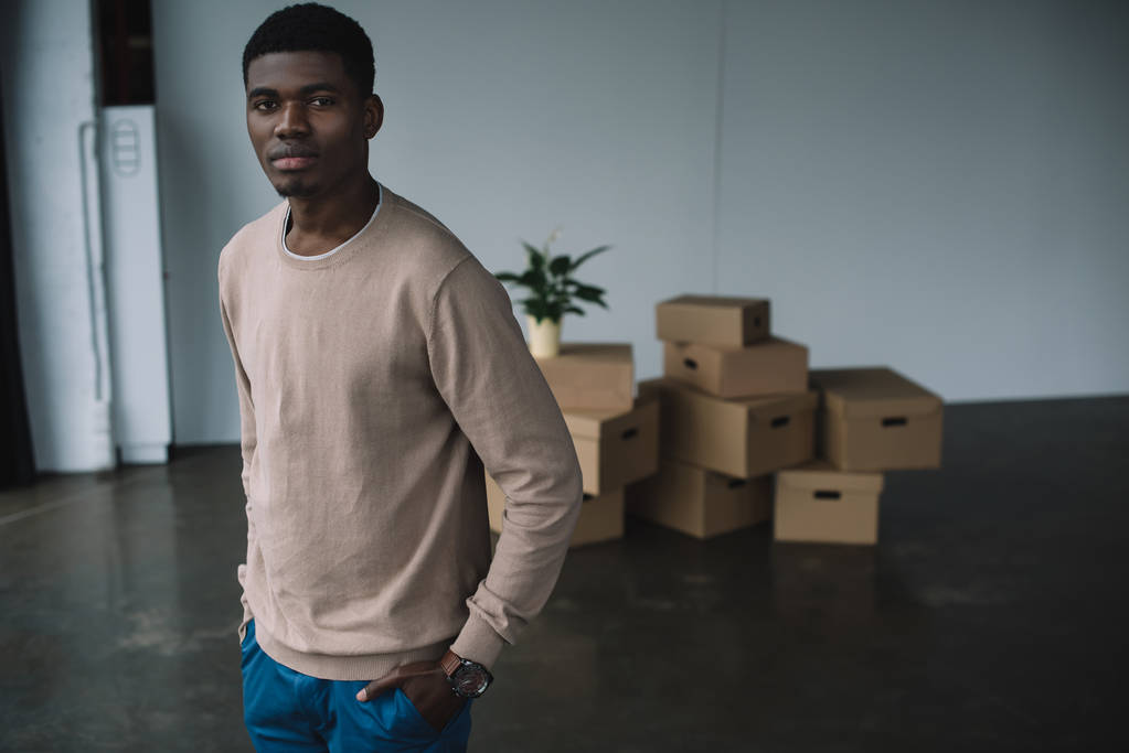 nuori afrikkalainen amerikkalainen mies seisoo kädet taskussa ja katselee kameraa muuttaessaan uuteen toimistoon
 - Valokuva, kuva