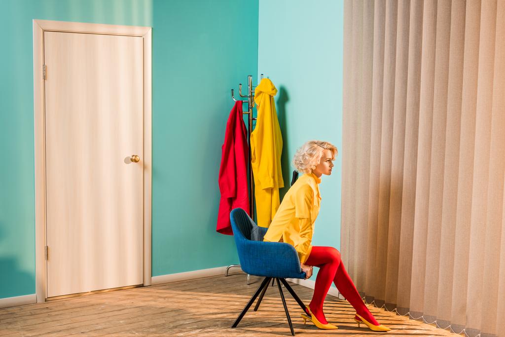 side view of pensive retro styled woman sitting on chair at bright apartment, doll house concept - Photo, Image