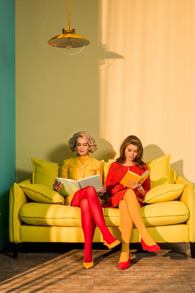 women in retro clothing reading books sitting on yellow sofa at bright apartment, doll house concept - Photo, Image