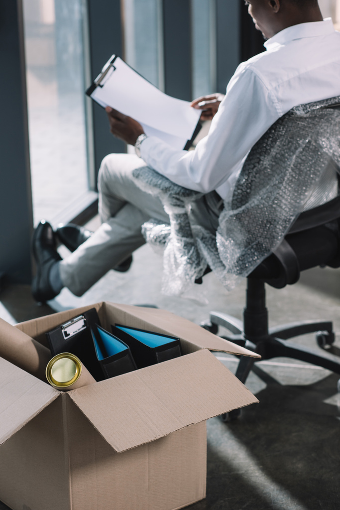 oříznutý snímek americký podnikatel drží schránky a lepenkové krabice s kancelářské potřeby na popředí - Fotografie, Obrázek