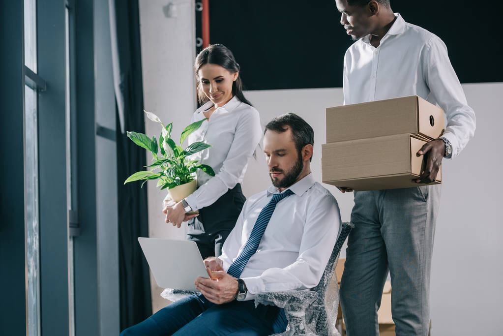 hommes d'affaires multiethniques avec ordinateur portable, boîtes et plantes en pot déménageant dans un nouveau bureau
 - Photo, image