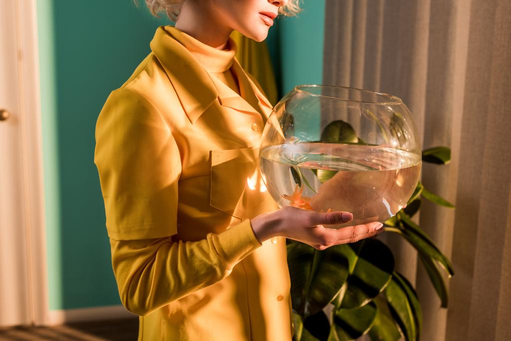 обрезанный образ стильной женщины, держащей аквариум с золотой рыбой дома
 - Фото, изображение