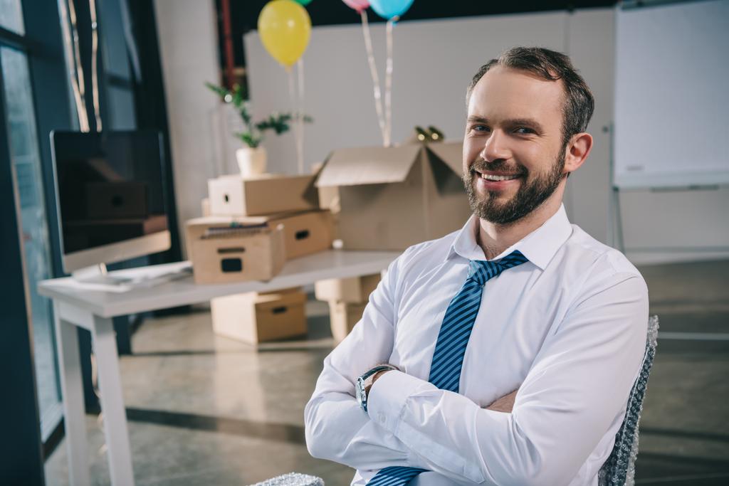 όμορφος επιχειρηματίας με σταυρωμένα χέρια χαμογελά στη φωτογραφική μηχανή στο νέο γραφείο, διακόσμηση με μπαλόνια - Φωτογραφία, εικόνα