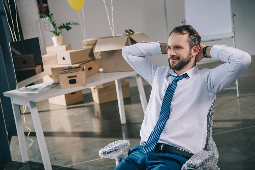 smiling businessman sitting with hands behind head in new office - Photo, Image