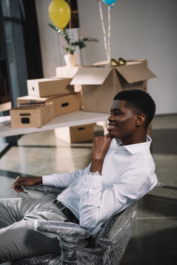 新事務所の職場で座っている若いアフリカ系アメリカ人実業家の笑みを浮かべてください。 - 写真・画像