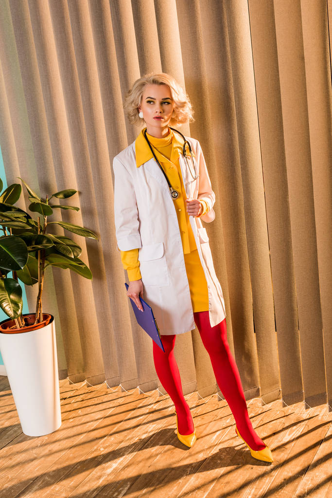 Schöne im Retro-Stil gestylte Ärztin in buntem Kleid mit Klemmbrett in Klinik - Foto, Bild
