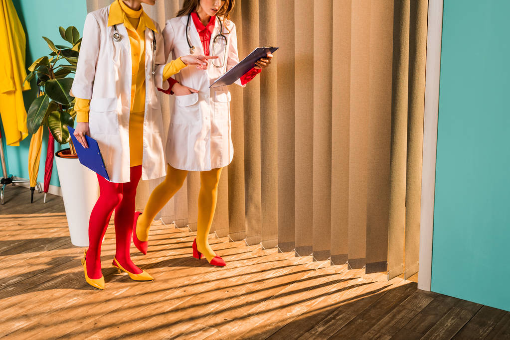 bijgesneden afbeelding van retro stijl artsen in kleurrijke panty's wijzen op Klembord in kliniek - Foto, afbeelding