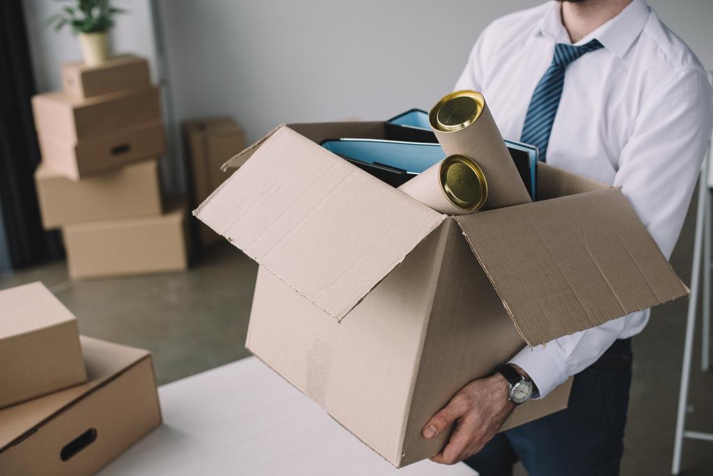 обрізаний знімок бізнесмена, що тримає картонну коробку з офісними приладдям
 - Фото, зображення