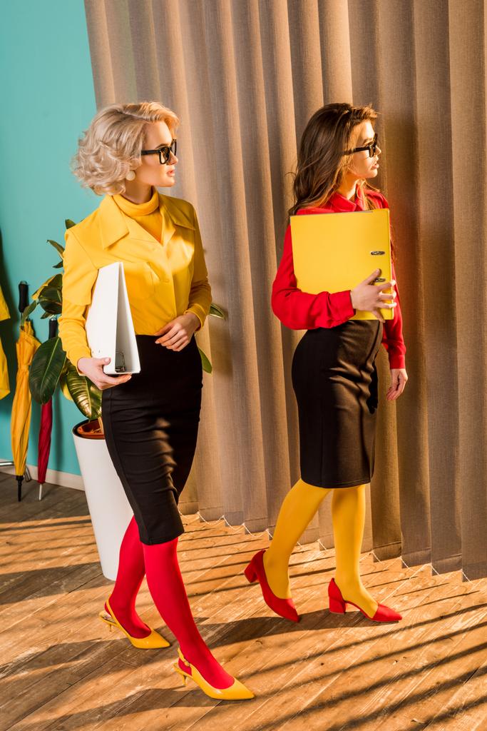 hermosas mujeres de negocios de estilo retro en coloridas blusas caminando con carpetas en la oficina
 - Foto, Imagen
