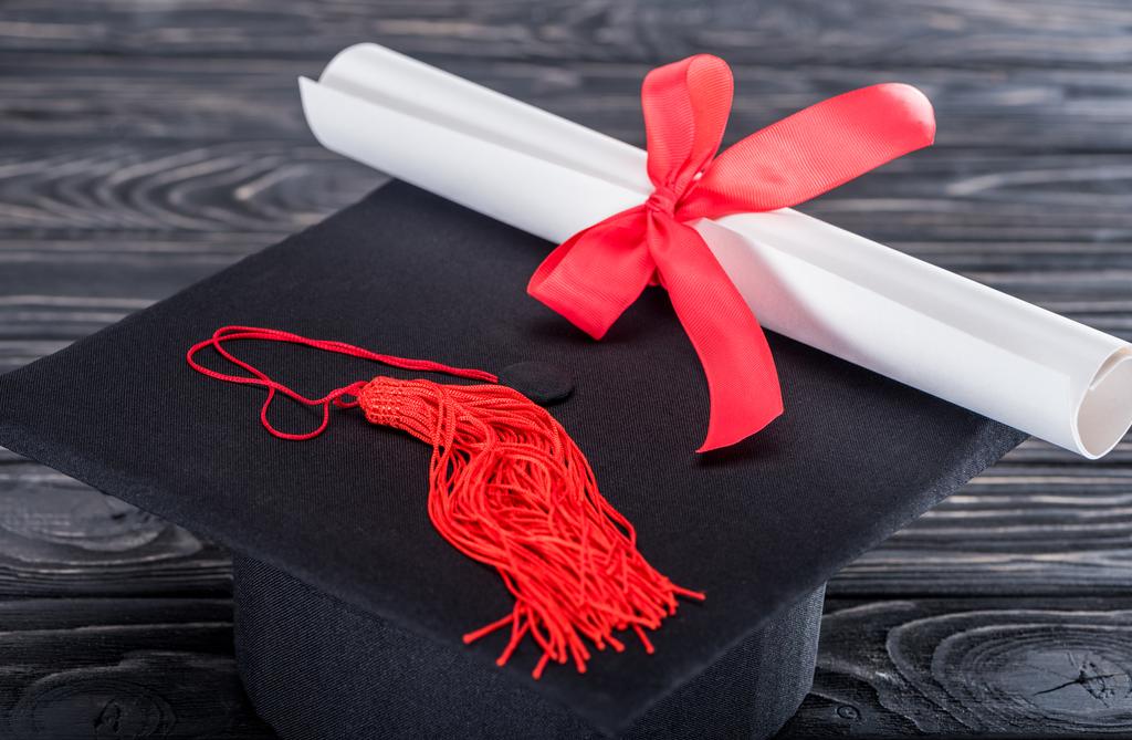 Chapéu de graduação e diploma com fita vermelha na mesa de madeira
 - Foto, Imagem