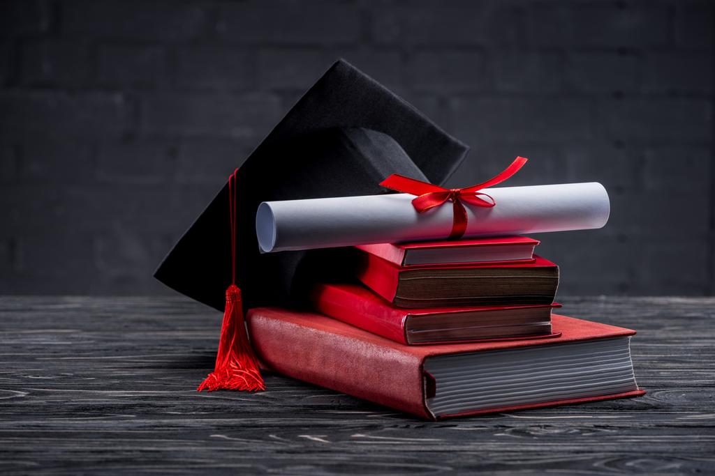 テーブルの上の卒業証書と卒業の帽子と書籍のスタック - 写真・画像
