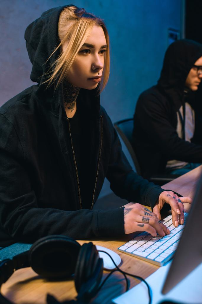жіночий хакер, що працює над новим шкідливим програмним забезпеченням зі спільницею в темній кімнаті
 - Фото, зображення