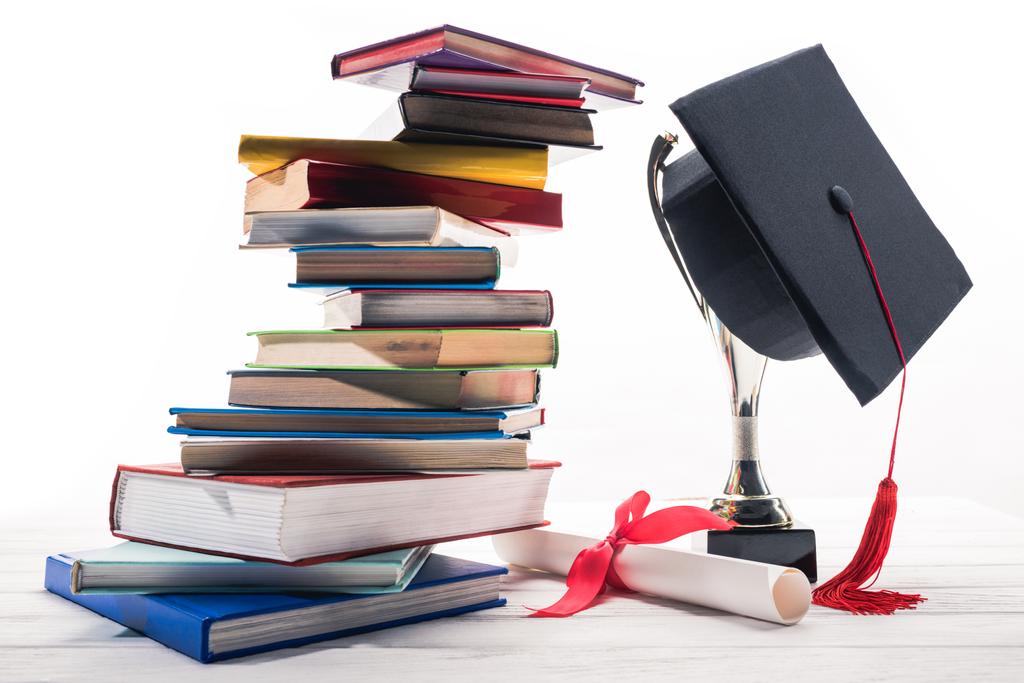 Graduiertenmütze auf Pokal nach Büchern und Diplom auf Tisch - Foto, Bild