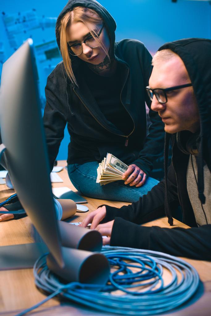 pareja de hackers con pila de dinero en efectivo en el lugar de trabajo
 - Foto, Imagen